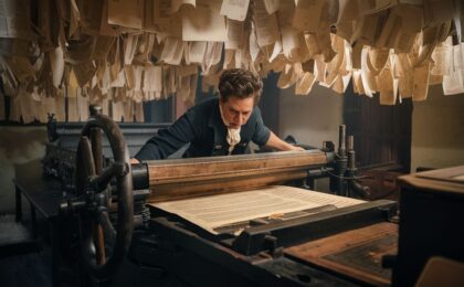 This AI generated image shows a man operating an 18th century printing machine, in a print shop with freshly printed documents hanging overhead to dry. This image was created to accompany a blog post titled "How do you build authority with content?".