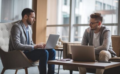 Image shows two people sitting with laptops , talking.